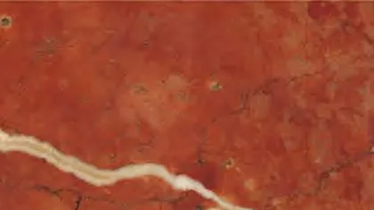 Rojo Alicante marble: saturated orange-red ground with a wide cream vein and small fossil marks