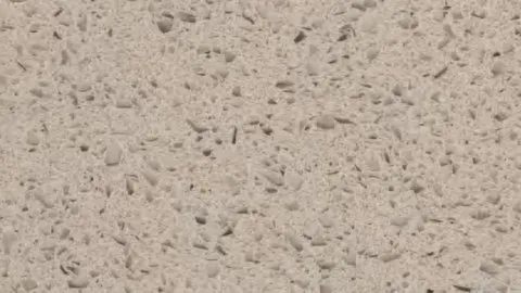 Sabbia Grano quartz slab: warm sand beige crowded with cream and translucent chips